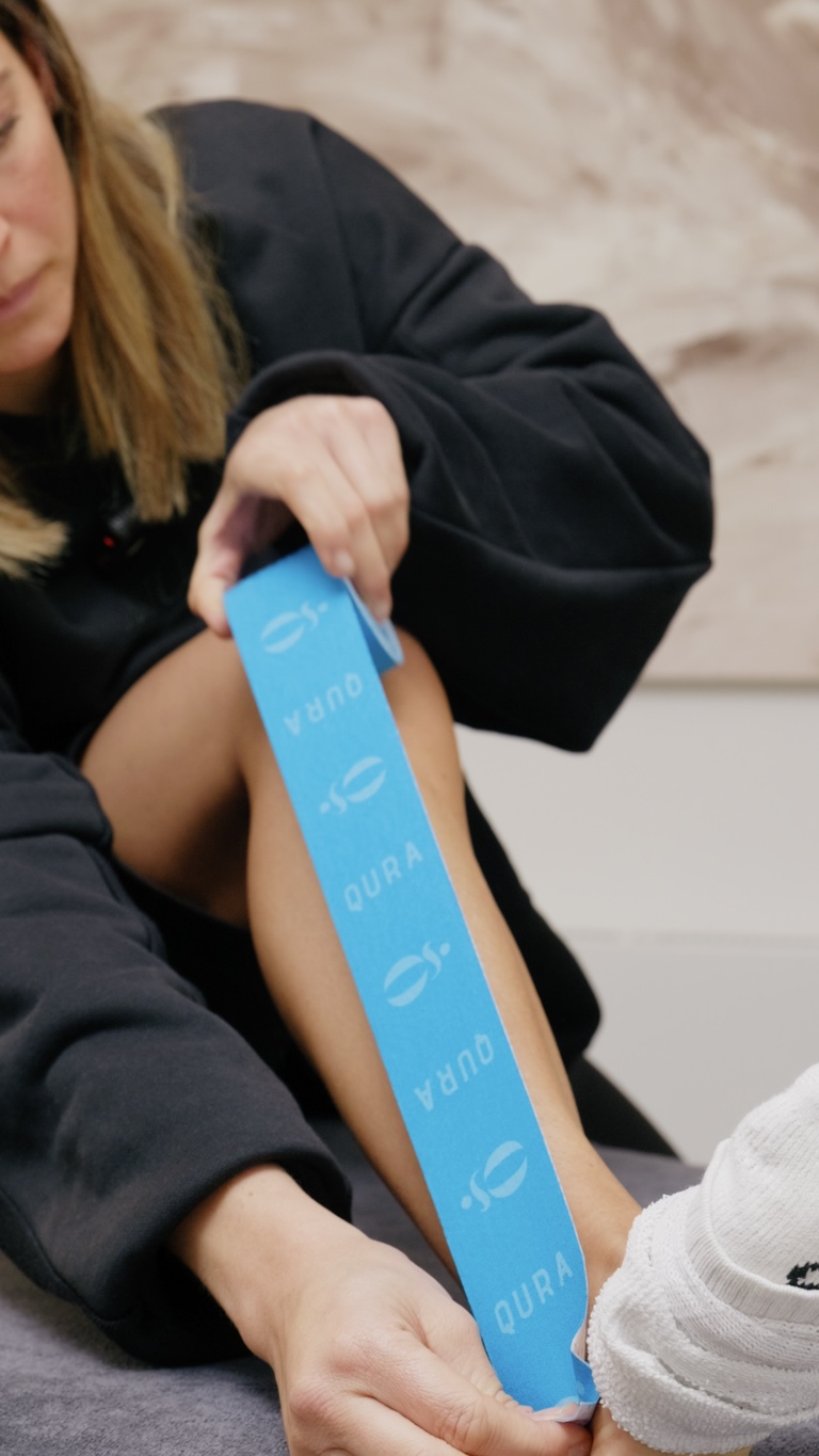 Sportlerin legt blaues Qura-Kinesio-Tape an der Wade an